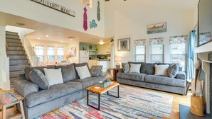 A spacious living room with two grey sofas, a wooden coffee table, and a colorful rug. A ceiling fan and a staircase are visible in the background. - Pet-friendly Condo w/ Seasonal Pool in Galveston! (Galveston)