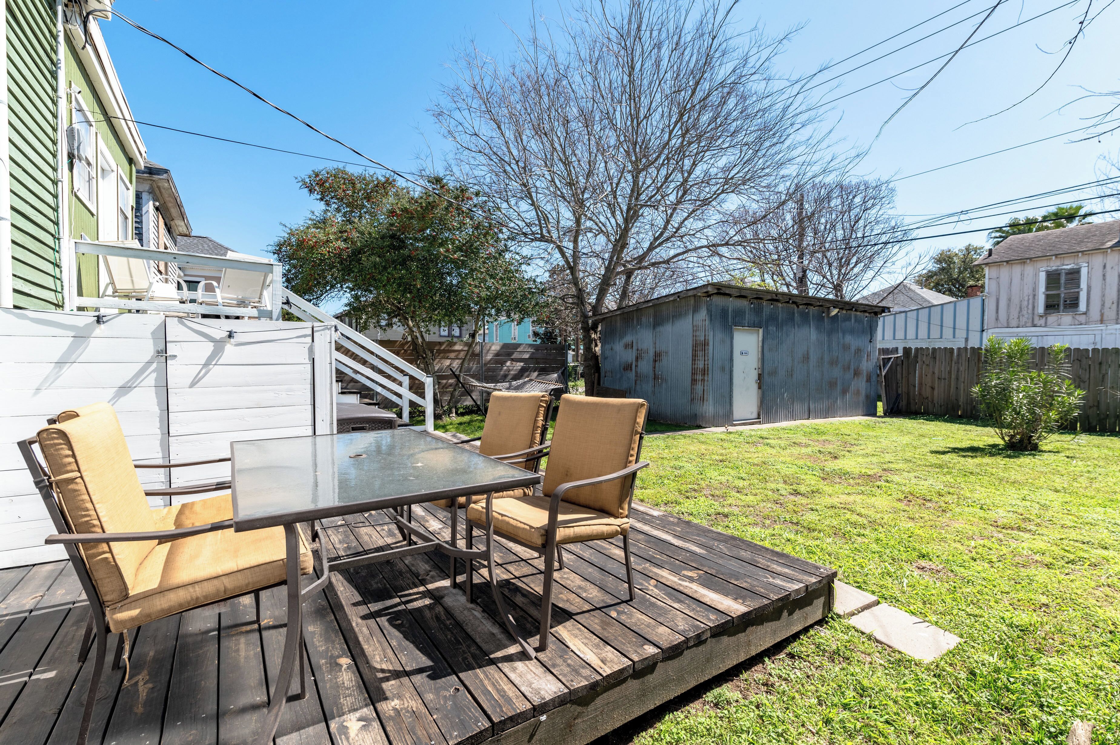 A wooden deck with a glass table and chairs, surrounded by a grassy yard and a wooden fence.