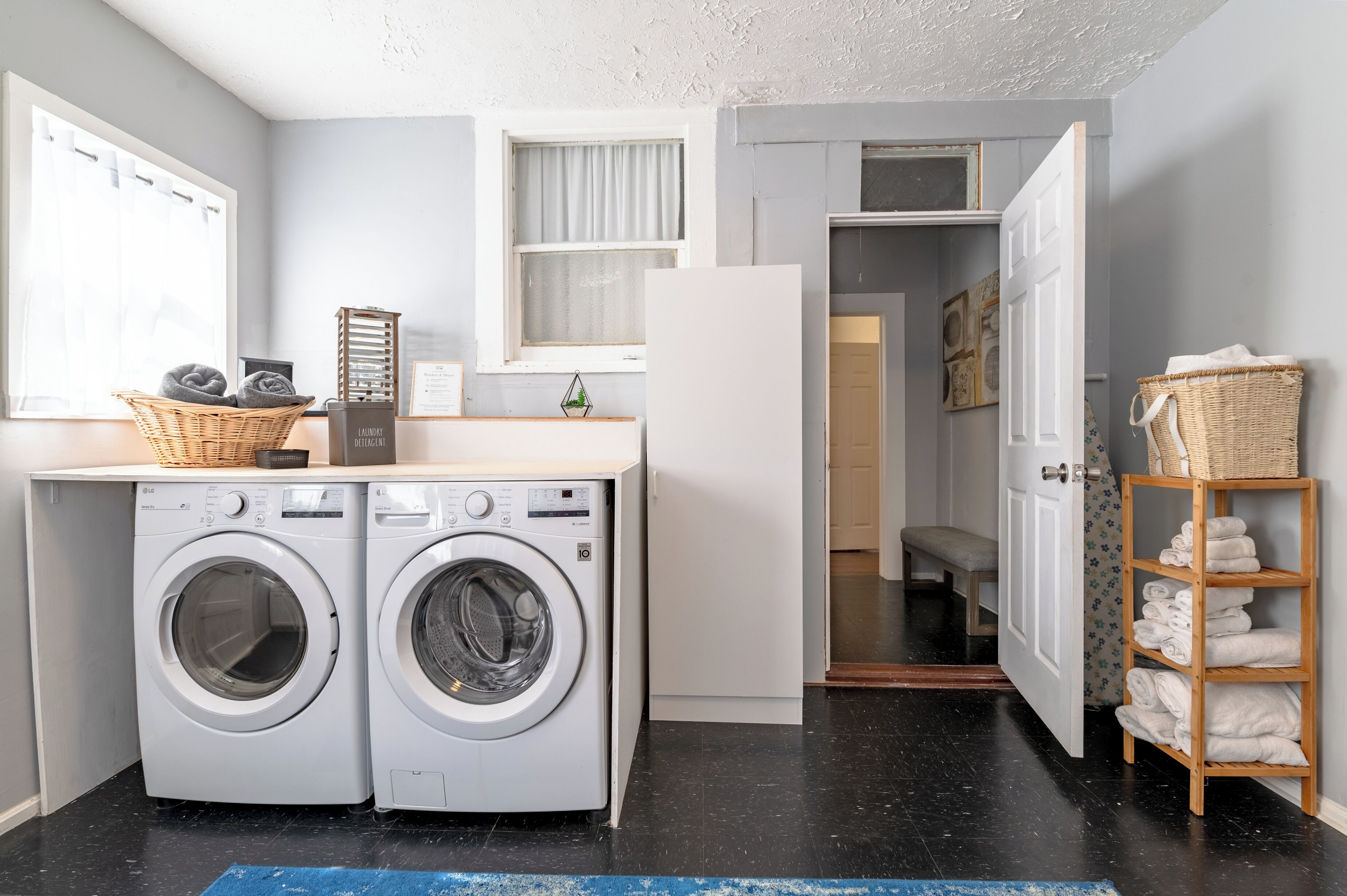 A laundry area with two front-loading washing machines, a drying rack, and a basket on the counter.