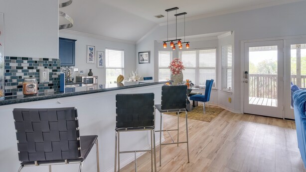 A modern kitchen with a central island, bar stools, and a dining area with a blue chair. - Furnished Patio & Deck: Galveston Escape! (Galveston)