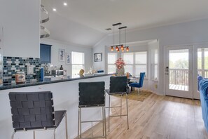 A modern kitchen with a central island, bar stools, and a dining area with a blue chair. - Furnished Patio & Deck: Galveston Escape! (Galveston)