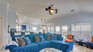 A modern living room with a blue sectional sofa, a glass coffee table, and a ceiling fan. - Furnished Patio & Deck: Galveston Escape! (Galveston)