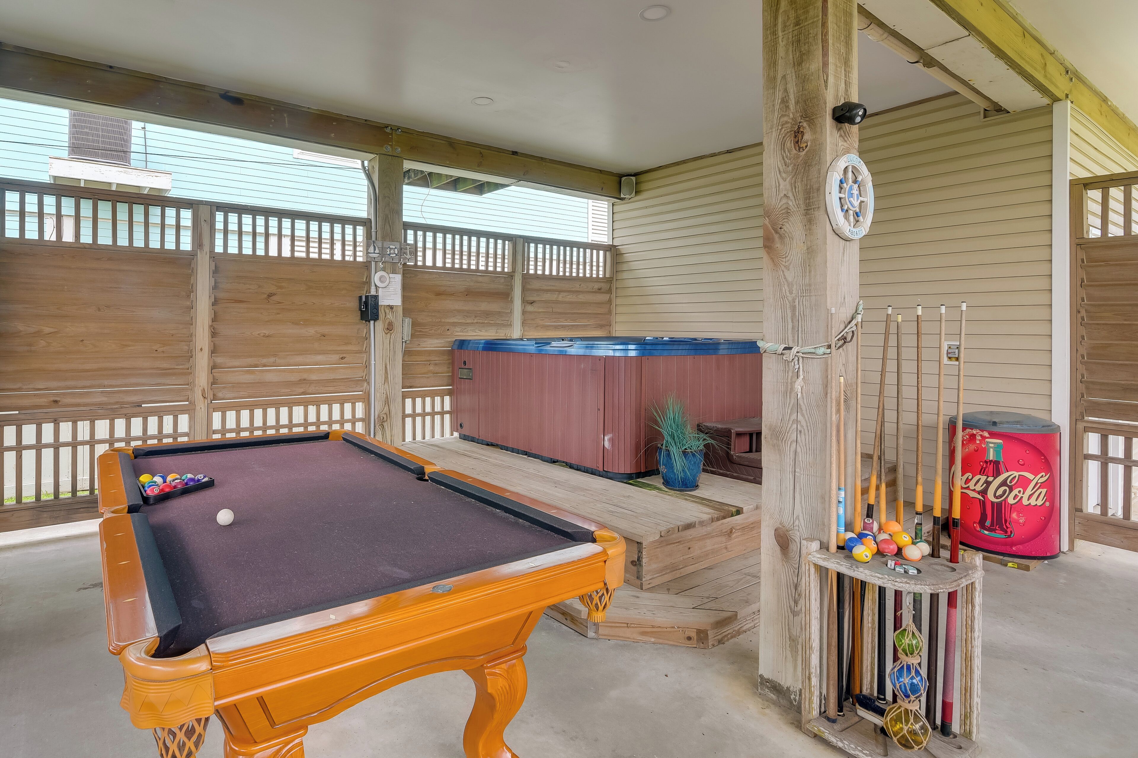 A pool table with balls, a wooden fence, a hot tub, and a Coca-Cola cooler.