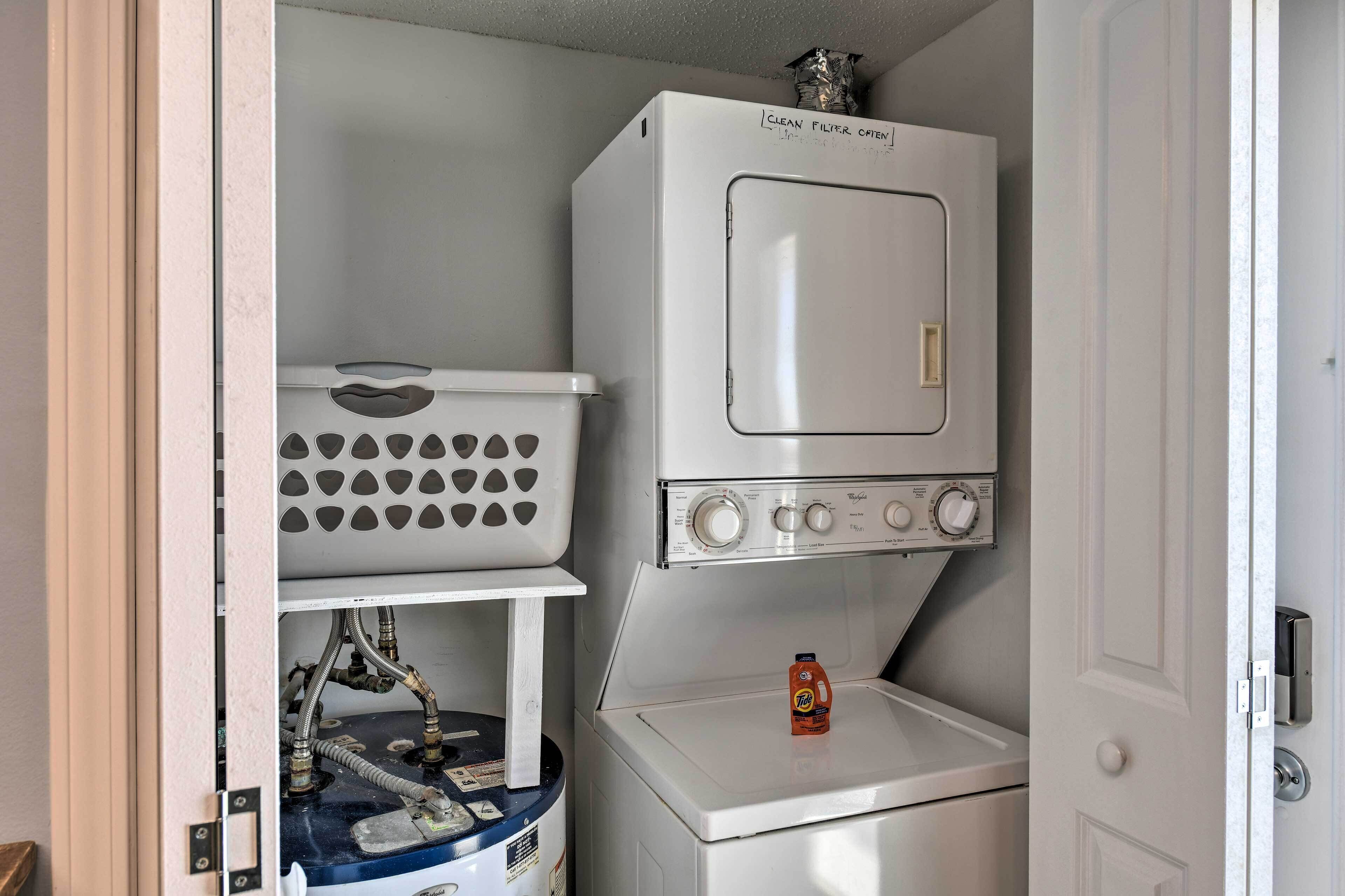 A compact laundry room with a front-loading washer and dryer, a storage basket, and a water heater.