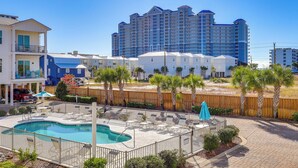 A hotel with a swimming pool, outdoor seating, and a view of a tall building in the background. - Gulf Shores Home w/ Shared Pool, 2 Blocks to Beach (Gulf Shores)