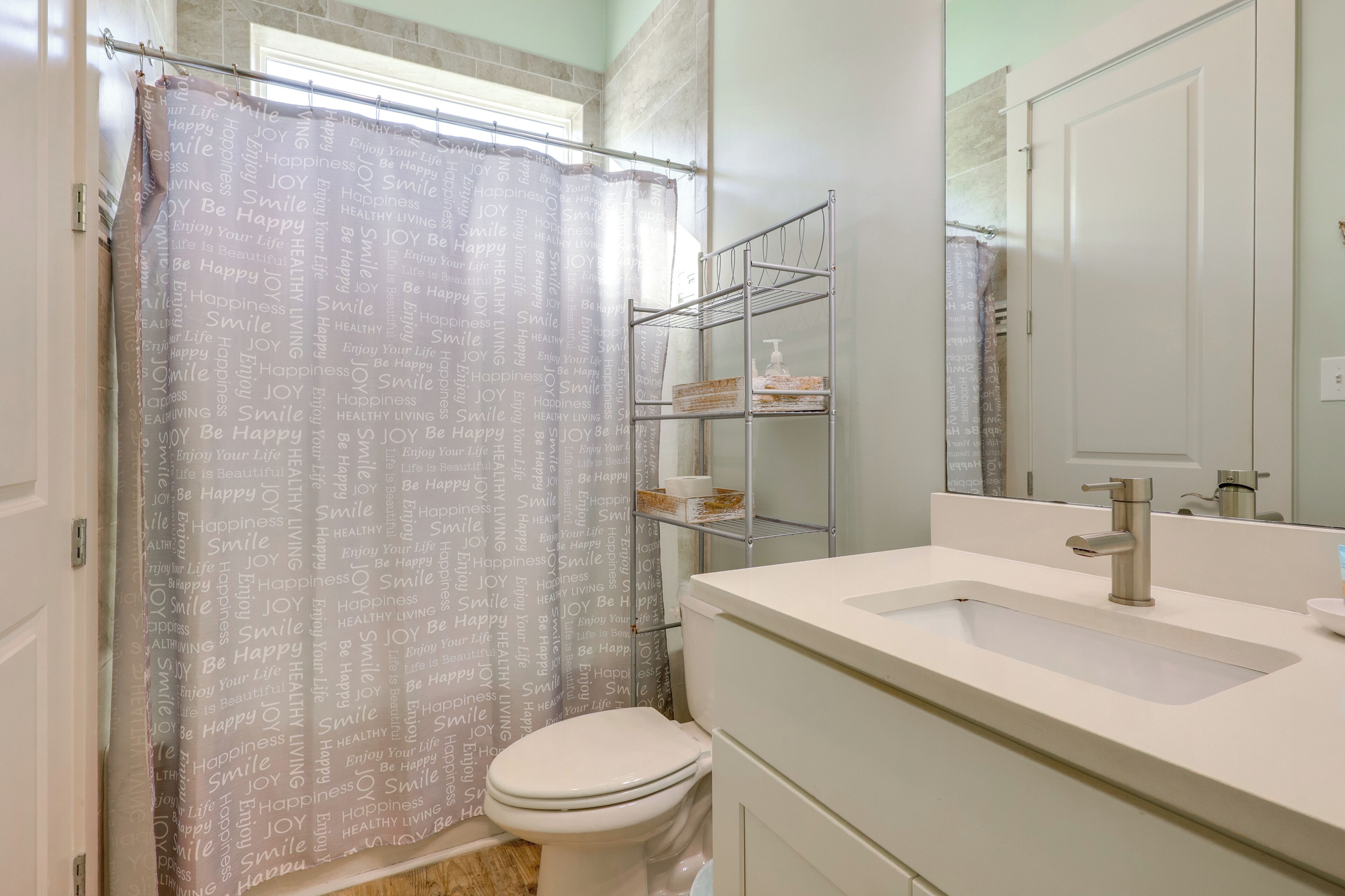 A bathroom with a shower curtain, a toilet, a sink, and a mirror.