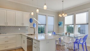 A modern kitchen with white cabinets, a glass island, and blue chairs. - Gulf Shores Home w/ Shared Pool, 2 Blocks to Beach (Gulf Shores)