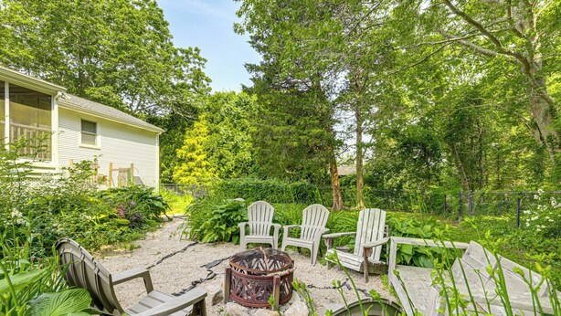 Eine Terrasse mit Adirondack-Stühlen, einer Feuerstelle und einem Haus im Hintergrund.