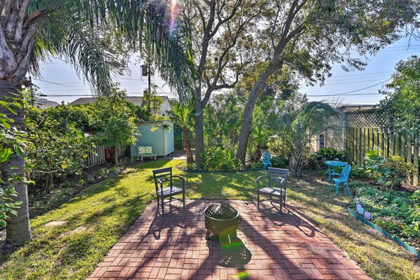 A backyard with a brick patio, two metal chairs, a metal table, and a metal fire pit. - Walk to Poretto Beach: Tropical Oasis in Galveston (Galveston)