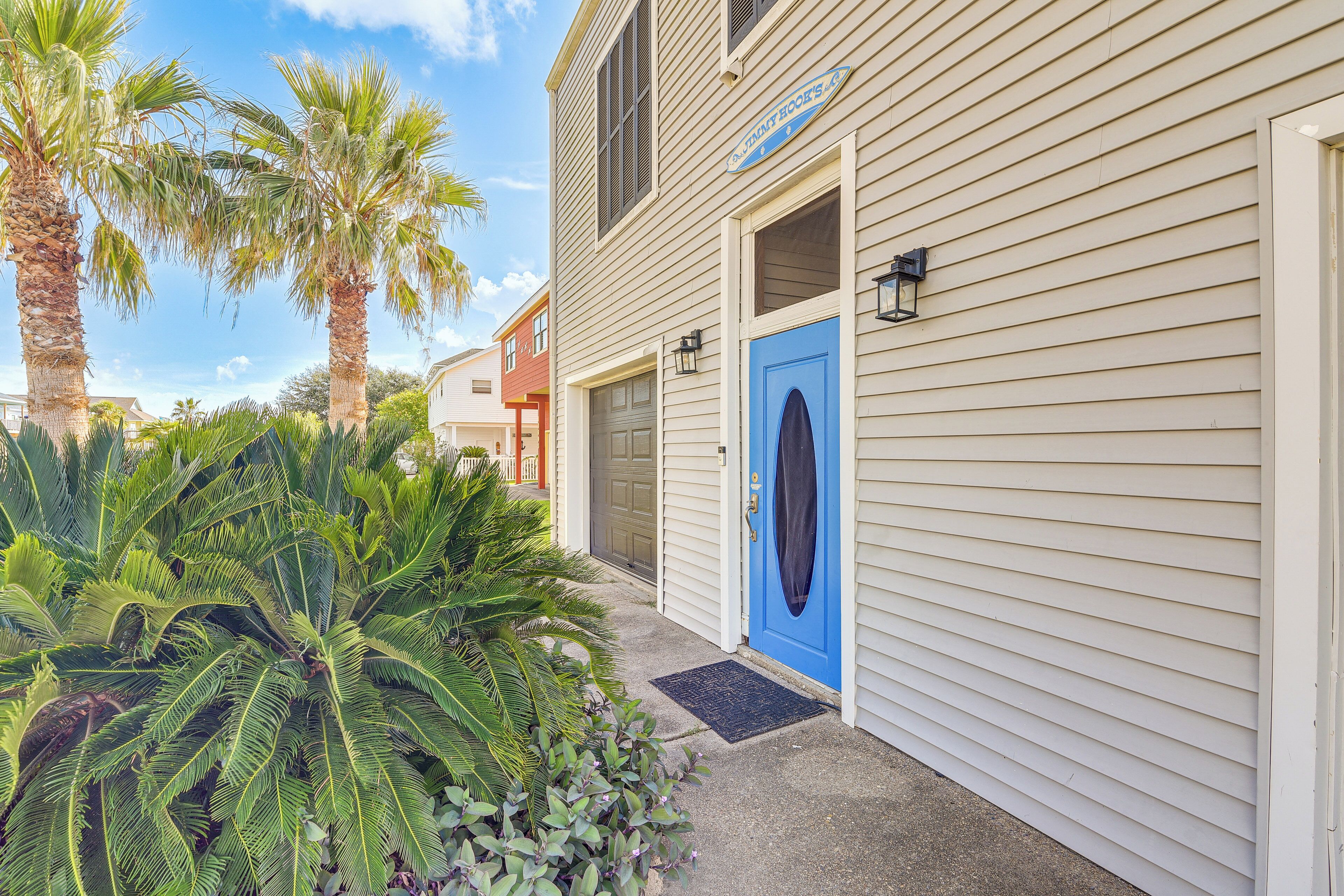 A building with a blue door, a sign above the door, and a palm tree in the foreground.