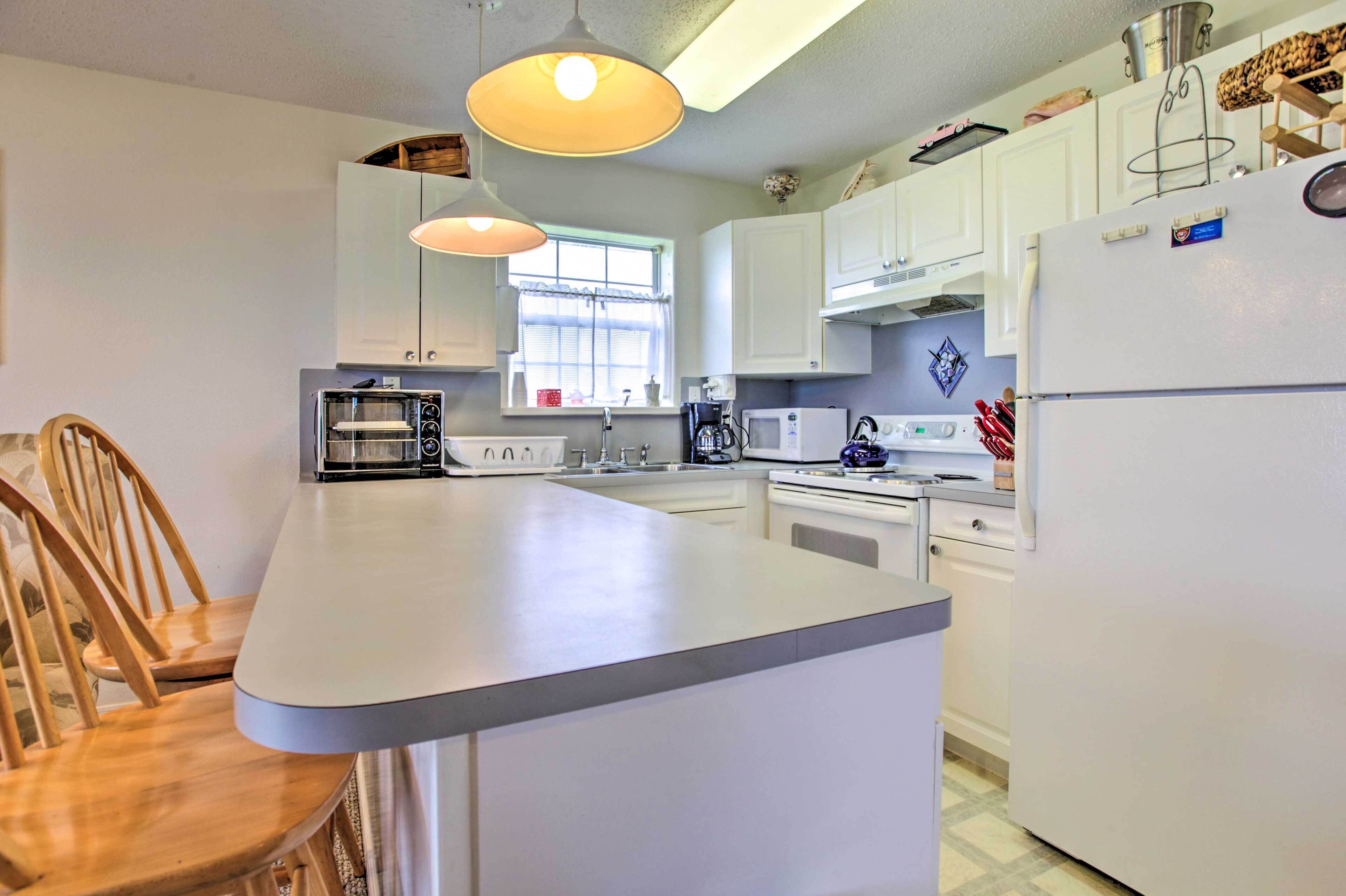 A modern kitchen with white cabinets, a central island, a microwave, a stove, and hanging utensils.