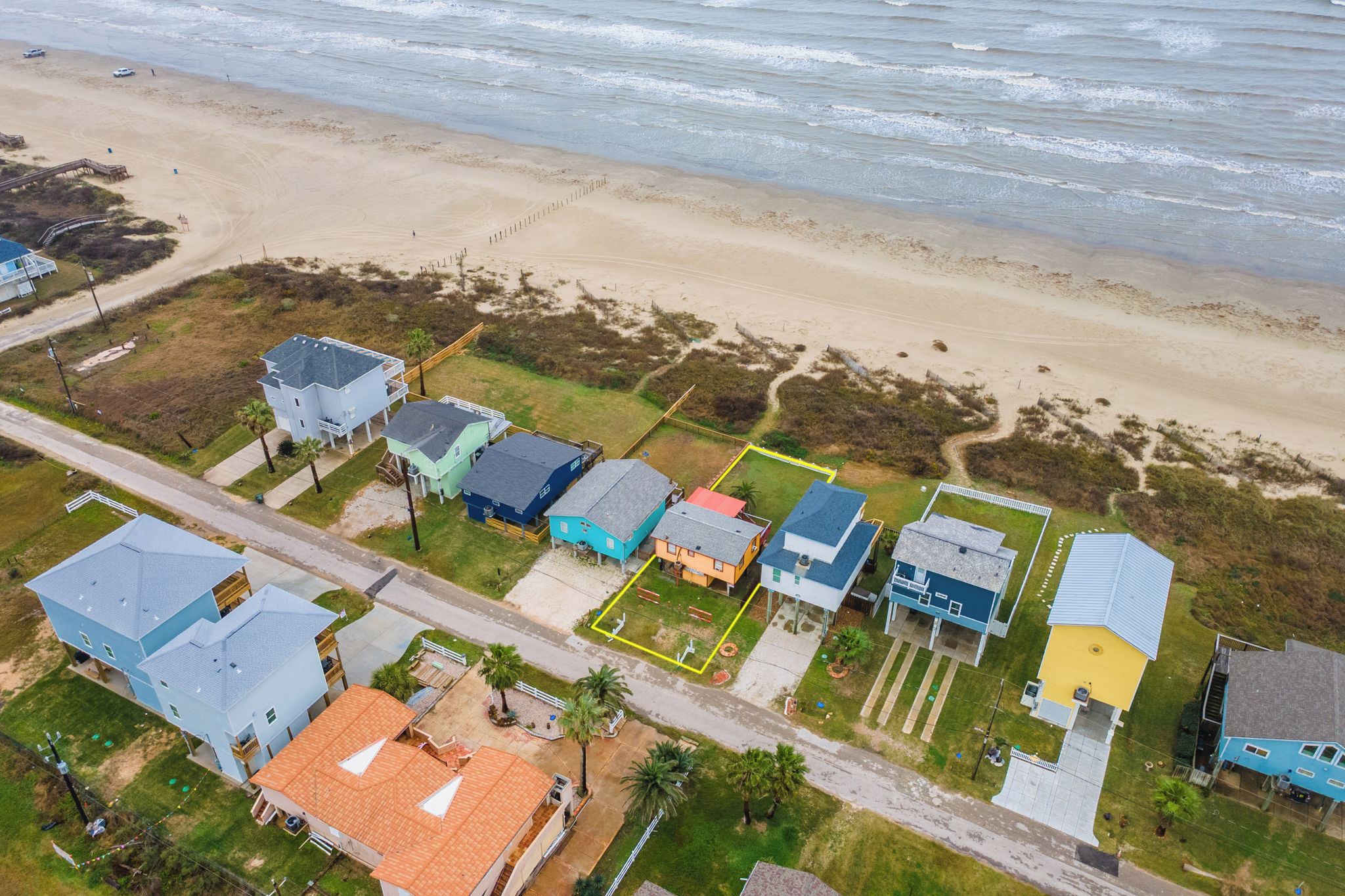 An aerial view of a coastal residential area with houses, a beach, and a road.