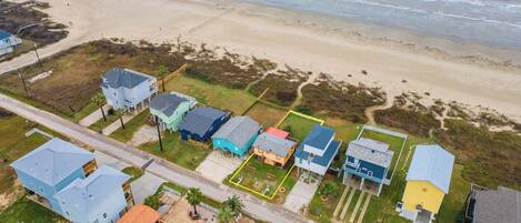 An aerial view of a coastal residential area with houses, a beach, and a road.
