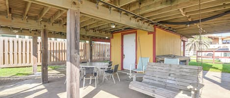 An outdoor covered patio with a table and chairs, a bench, and a swing.