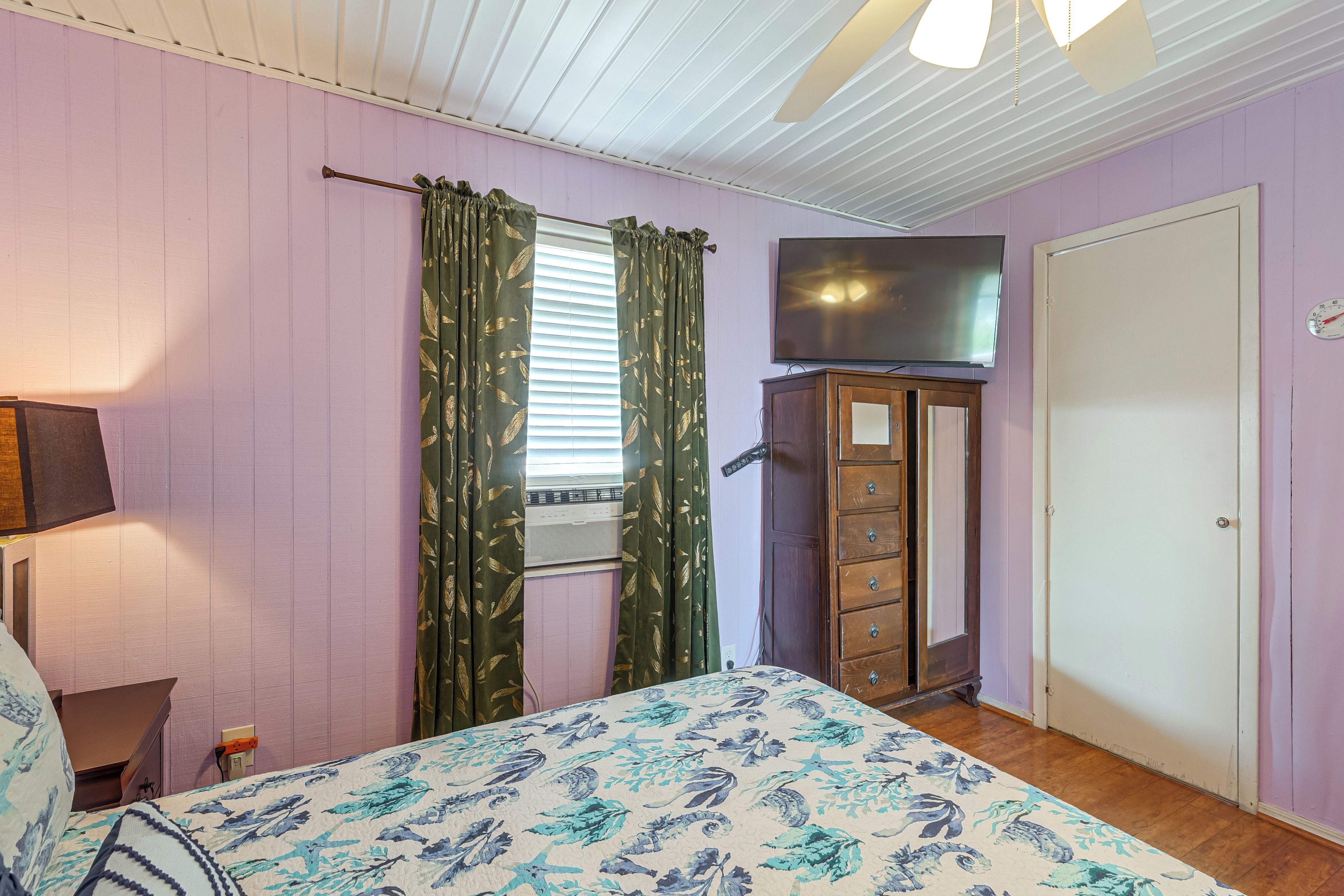 Ein Schlafzimmer mit einem Bett, einem Schminktisch, einem Fernseher und einem Fenster mit Vorhängen.