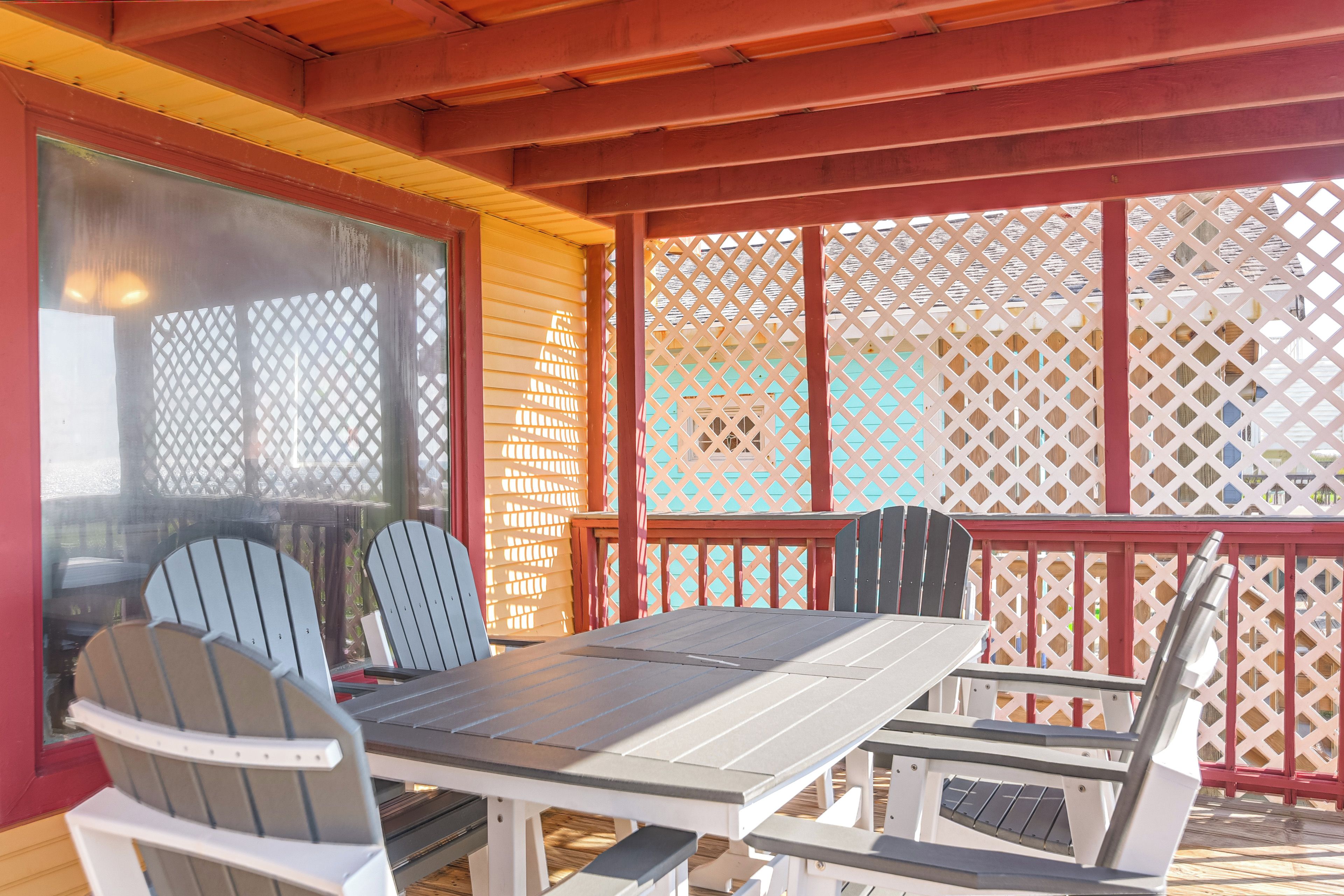 A covered outdoor seating area with a table and chairs, a view of the surrounding area, and a lattice fence.