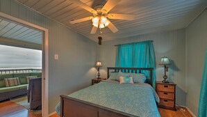 A bedroom with a wooden bed, a ceiling fan, a nightstand with a lamp, and a view of a balcony.