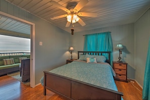 A bedroom with a wooden bed, a ceiling fan, a nightstand with a lamp, and a view of a balcony.