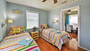 A bedroom with two beds, a ceiling fan, a window with blinds, and a door leading to another room. - Steps to Gulf! Pet-friendly Galveston Getaway (Galveston)