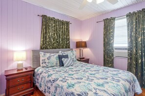 A bedroom with a bed, nightstands, a lamp, and curtains. - Steps to Private Beach! Pet-friendly Getaway (Galveston)