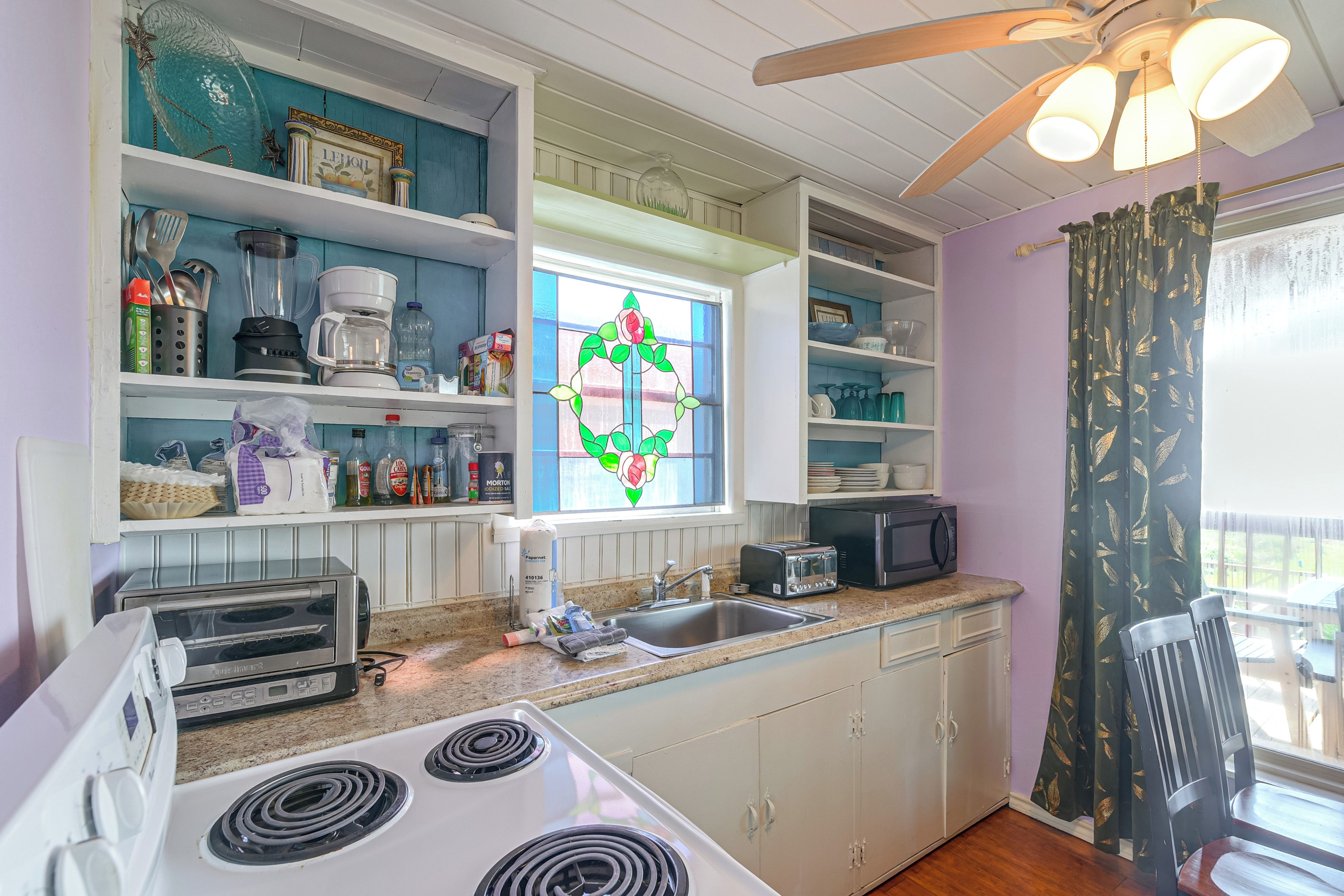 A kitchen with a stove, toaster, sink, and various kitchen items on shelves.