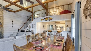 A dining area with a wooden table set for six, surrounded by wooden chairs. A staircase with a railing leads to an upper level. - Waterfront Lay Lake Retreat w/ Dock & 3 Piers! (Shelby)