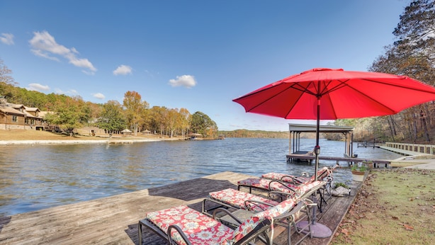 A wooden dock with lounge chairs and a red umbrella, overlooking a calm lake with trees and a dock in the background. - Waterfront Lay Lake Retreat w/ Dock & 3 Piers! (Shelby)
