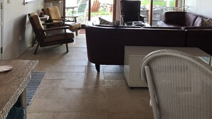 Un soggiorno con soffitto in legno, un divano in pelle marrone, una poltrona in vimini bianco e un televisore su un mobile.