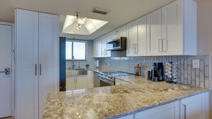 A modern kitchen with white cabinetry, a granite countertop, a built-in microwave, and a ceiling light fixture. - Cozy Condo w/ Gulf View, Bird Watching + Telescope (Hudson)