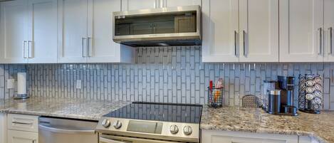 A modern kitchen with white cabinets, a stainless steel microwave, a gas stove, and a built-in oven.
