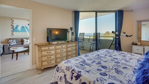 A bedroom with a large bed, a dresser, a television, and a balcony with a telescope. - Cozy Condo w/ Gulf View, Bird Watching + Telescope (Hudson)