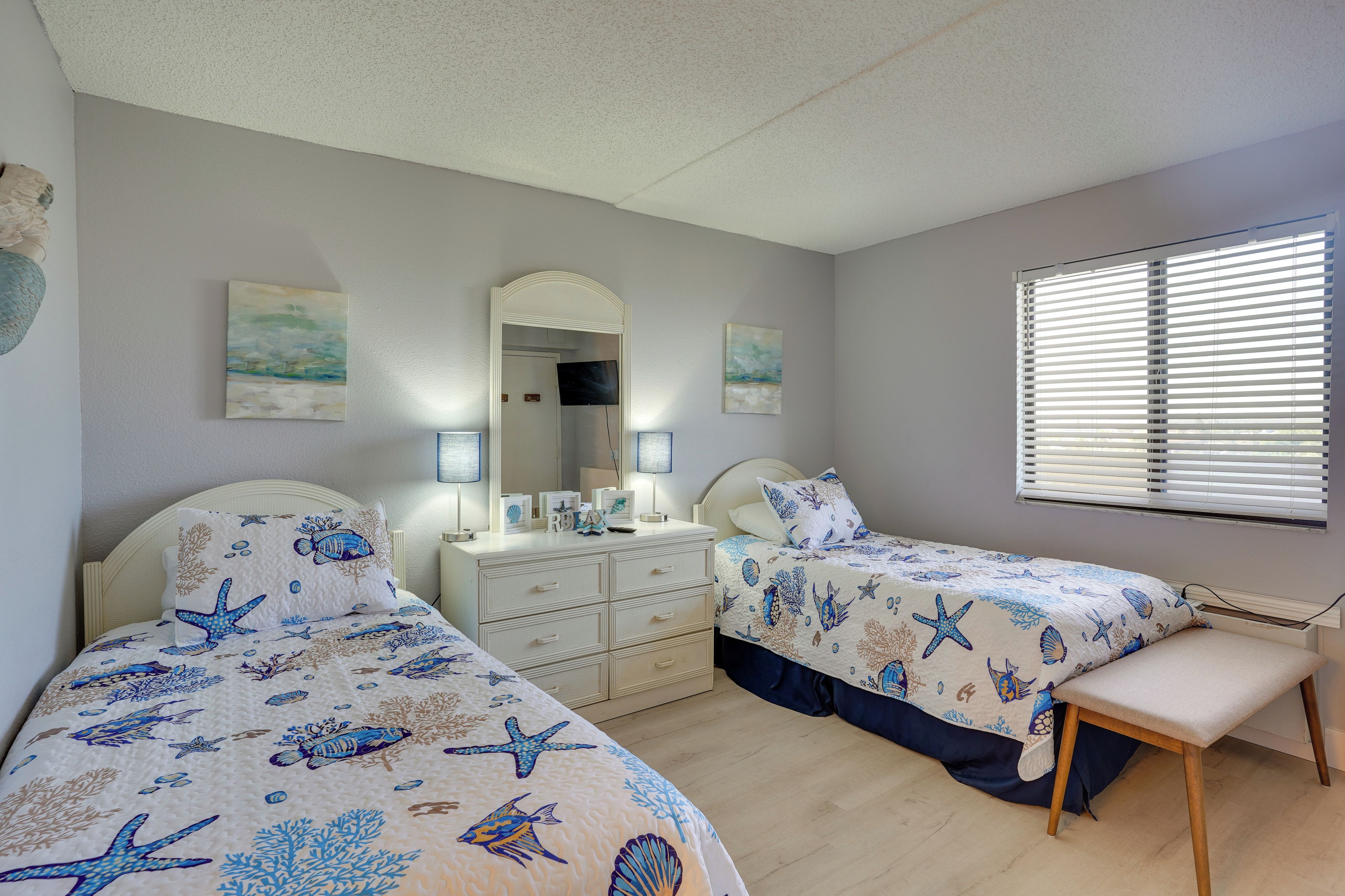 A bedroom with two beds, a nightstand, a dresser, and a window with blinds.