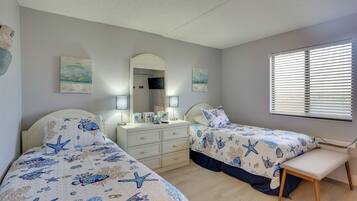 A bedroom with two beds, a nightstand, a dresser, and a window with blinds.