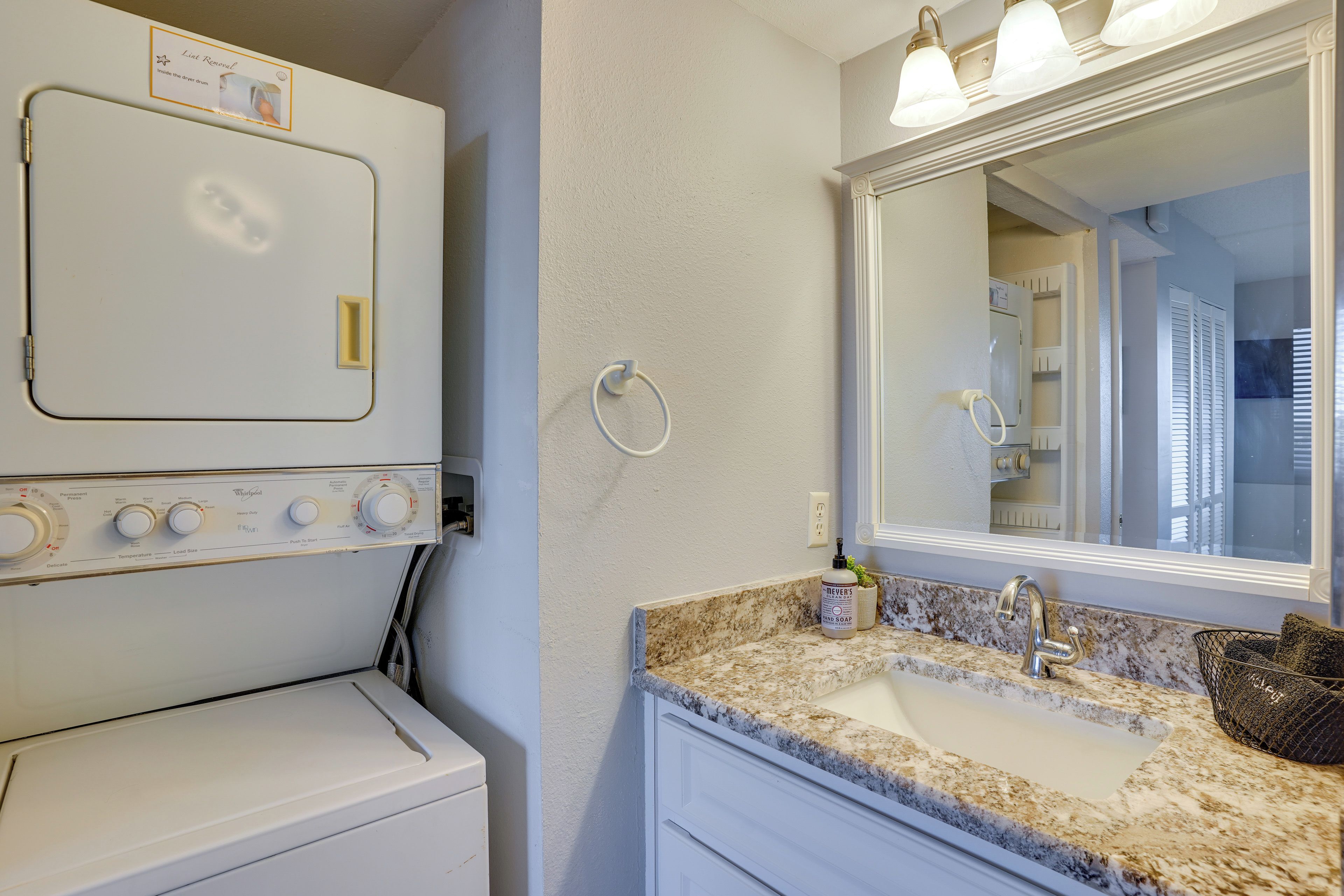 A bathroom with a white washing machine, a sink with a marble countertop, and a large mirror.