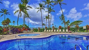 A swimming pool with a curved edge, surrounded by palm trees and lounge chairs.