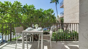 A balcony with a table set for dining, surrounded by lush greenery and a clear blue sky.