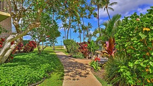 A pathway flanked by lush greenery and palm trees, leading to a building with a balcony.