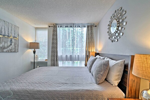 A bedroom with a large bed, a mirror, and a window with curtains. - Kailua-kona Condo w/ Lanai, Walk to Beach + Pier! (Kailua-Kona)
