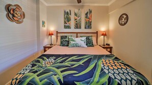 Un dormitorio con cama, dos mesitas de noche, ventilador de techo y decoración en la pared.