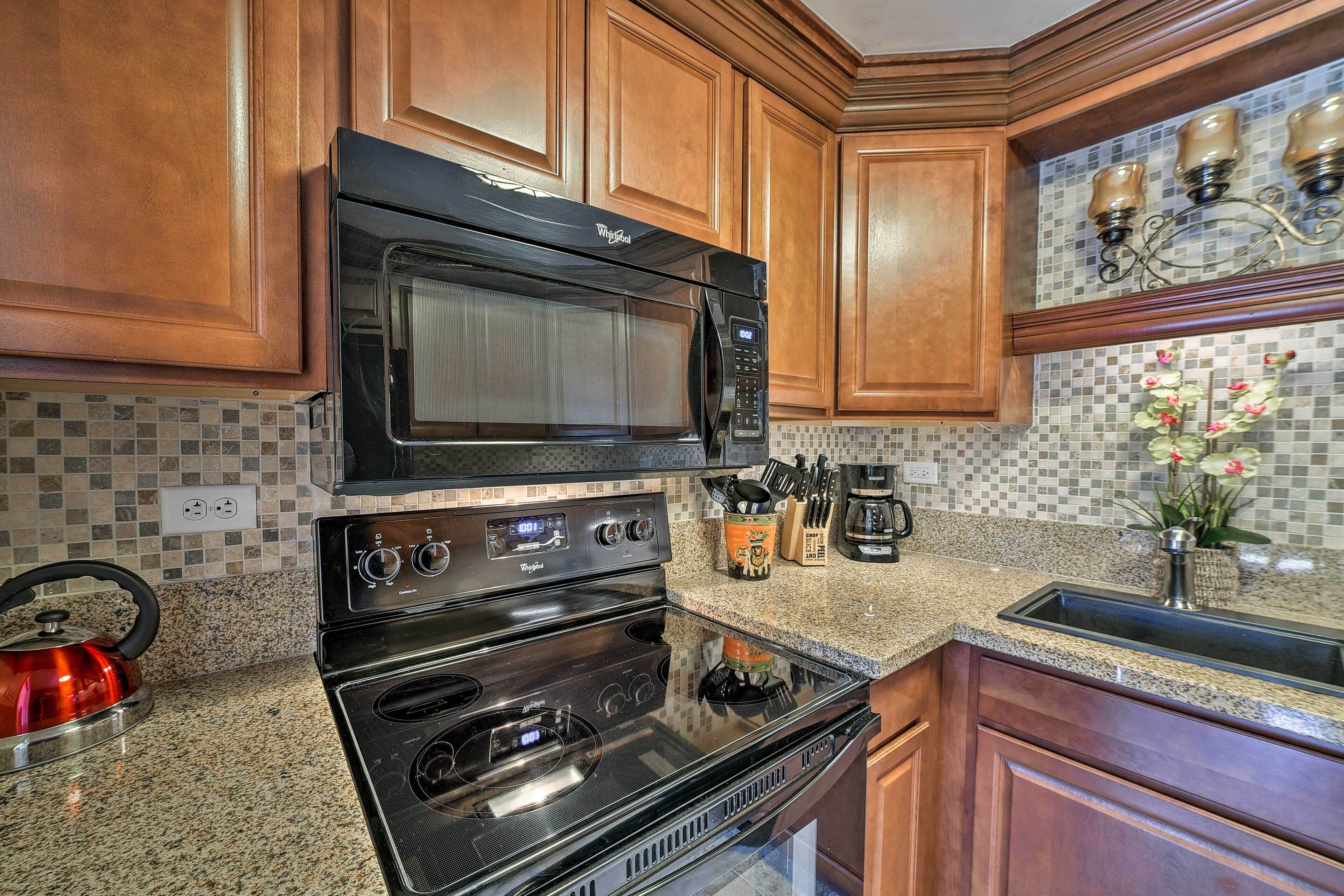 A kitchen with wooden cabinets, a black microwave, a stove, and a granite countertop.
