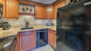 Una cocina con armarios de madera, un refrigerador negro, un lavavajillas, una cafetera y un tostador.