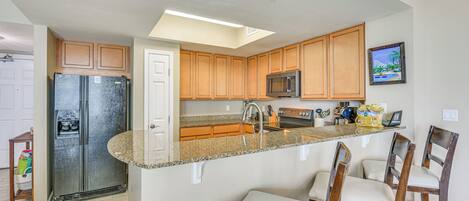 Una cocina con armarios de madera, un refrigerador de acero inoxidable, un microondas y una encimera de granito.