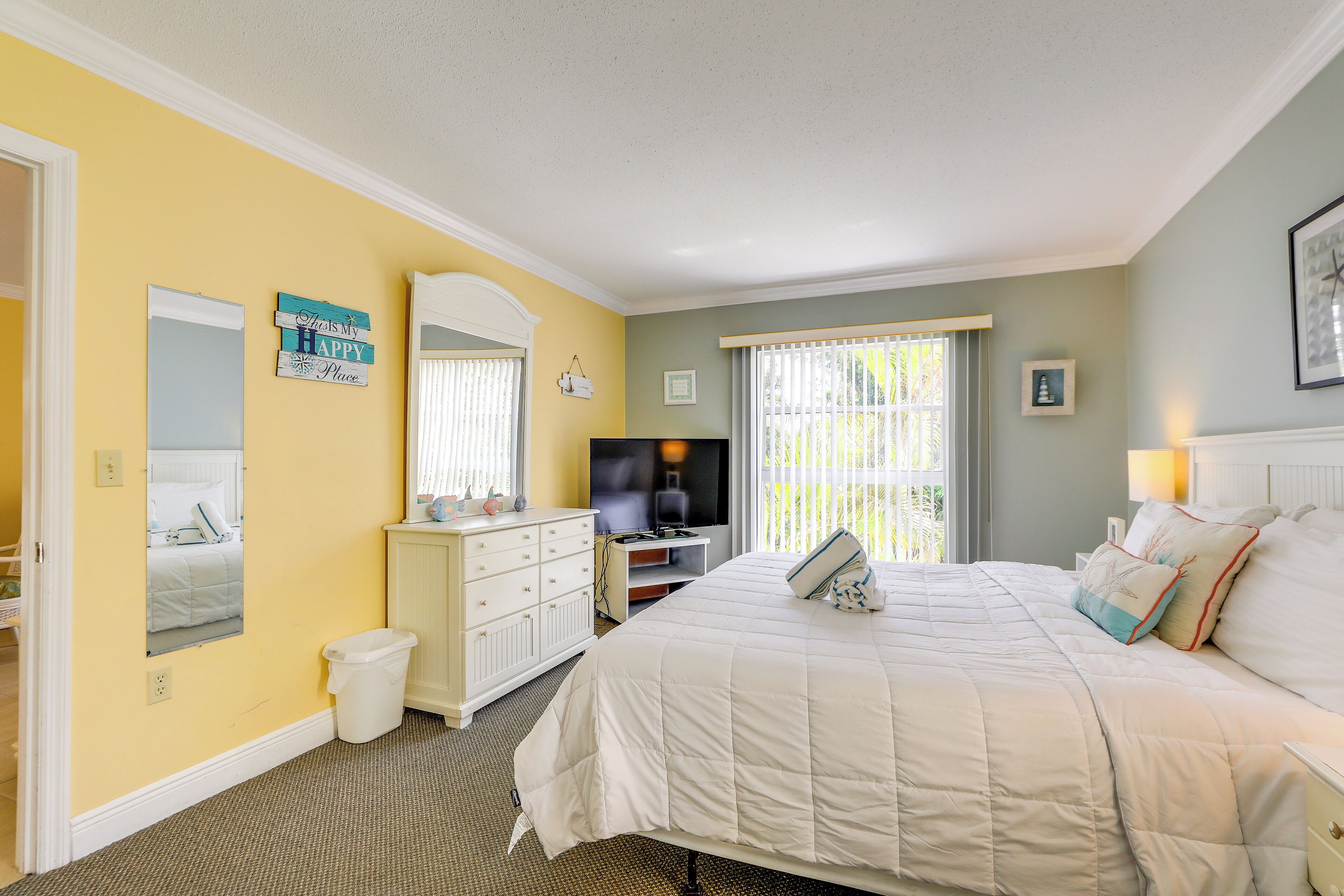 A bedroom with a bed, a television, a desk, and a window with blinds.