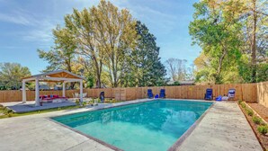 A rectangular swimming pool with a wooden deck surrounding it, a covered seating area with a red and white couch, and a wooden fence. - Gulf Breeze Home w/ Pool, Grill & Fire Pit (Gulf Breeze)