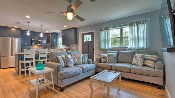 A modern kitchen with dark cabinets, a white dining table, and a ceiling fan. There are two gray sofas with patterned cushions and a small white table with a green vase. - Gulf Breeze Home w/ Pool, Grill & Fire Pit (Gulf Breeze)