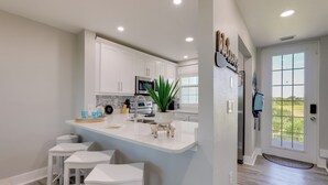 A modern kitchen with white cabinets, a central island with stools, a microwave, and a potted plant.