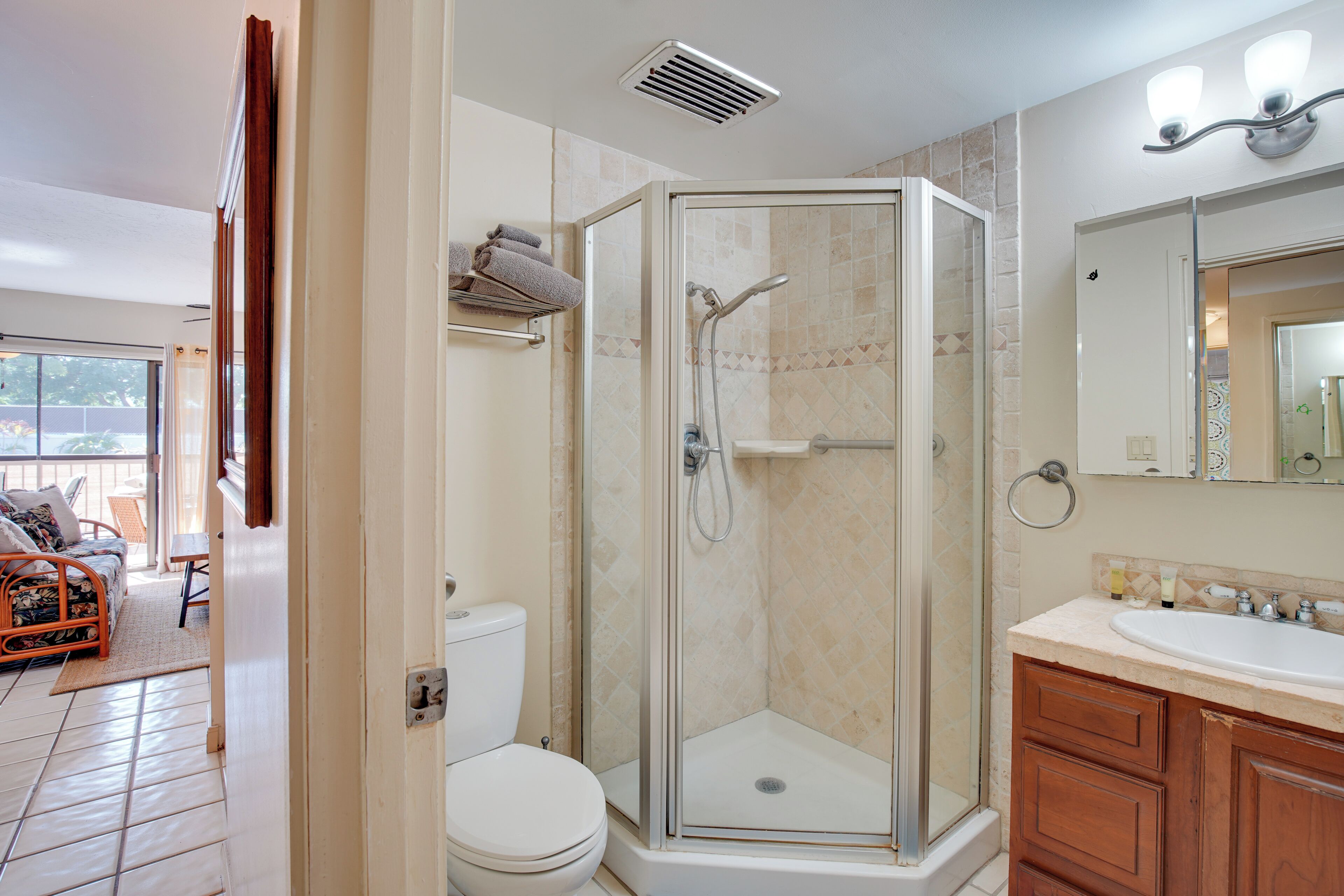 A bathroom with a glass-enclosed shower, a toilet, and a sink with wooden cabinets.