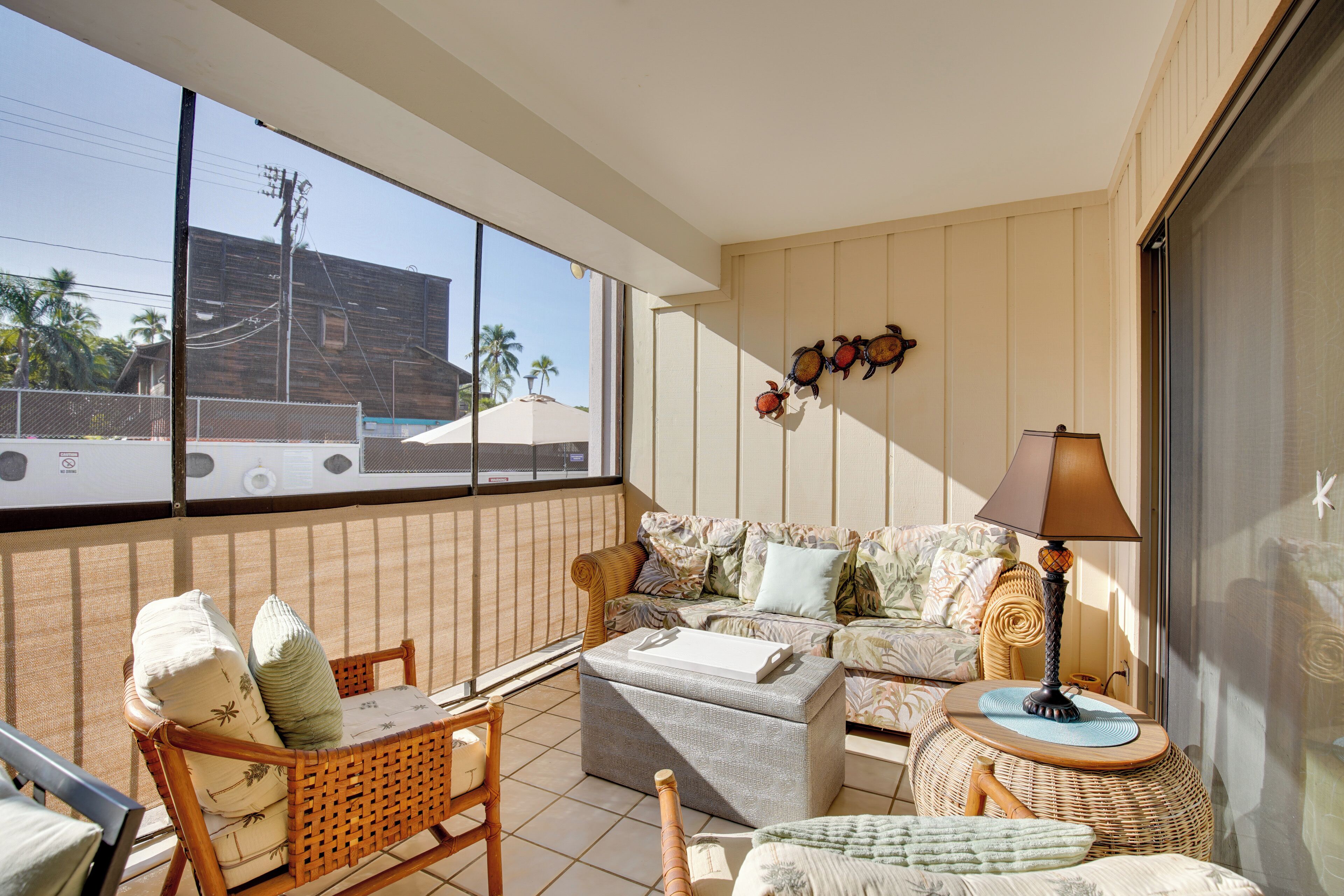 A sunlit balcony with wicker furniture, a cushioned sofa, and a small round table with a lamp.