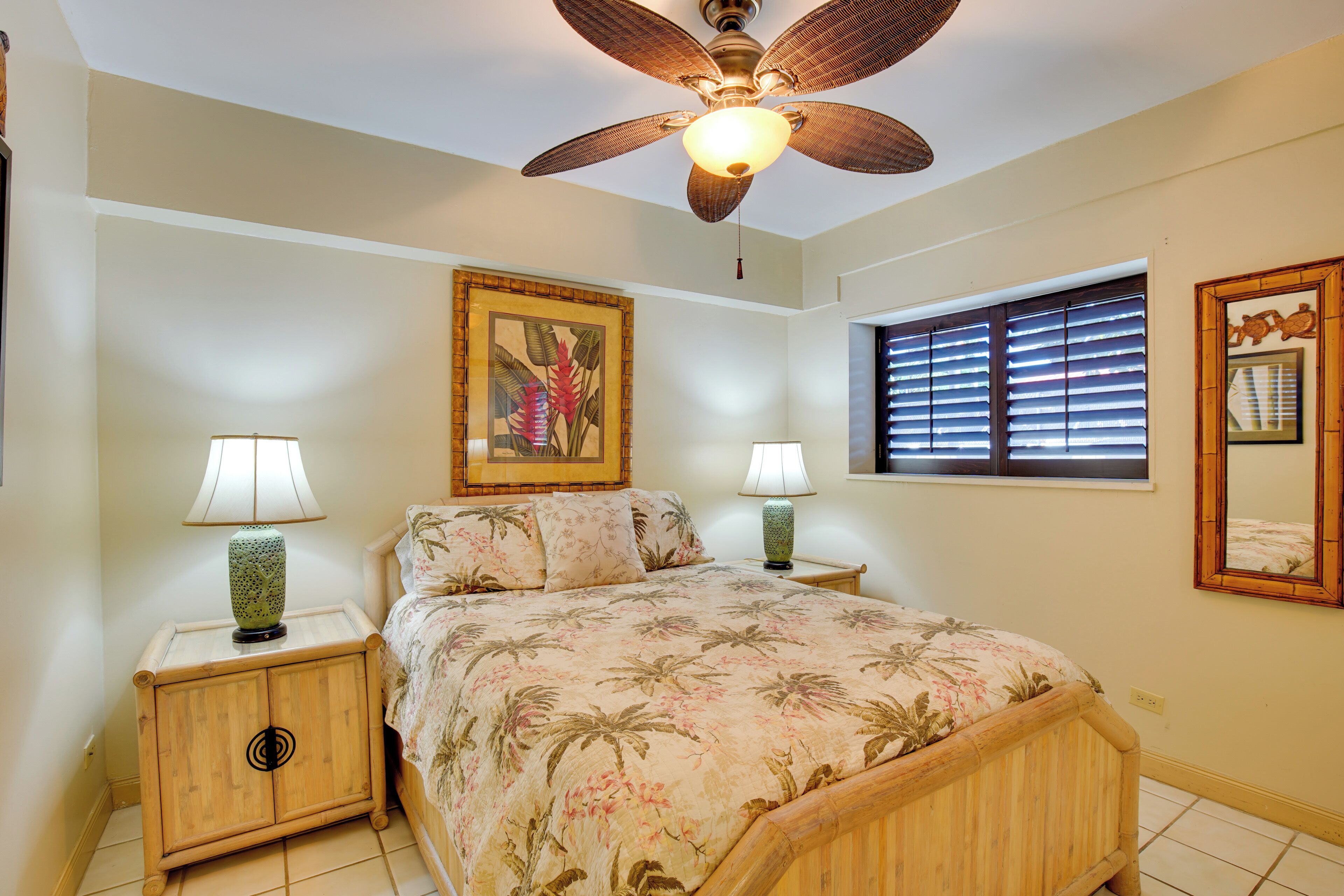 A bedroom with a bed, two nightstands, a ceiling fan, a window with blinds, and a framed picture on the wall.