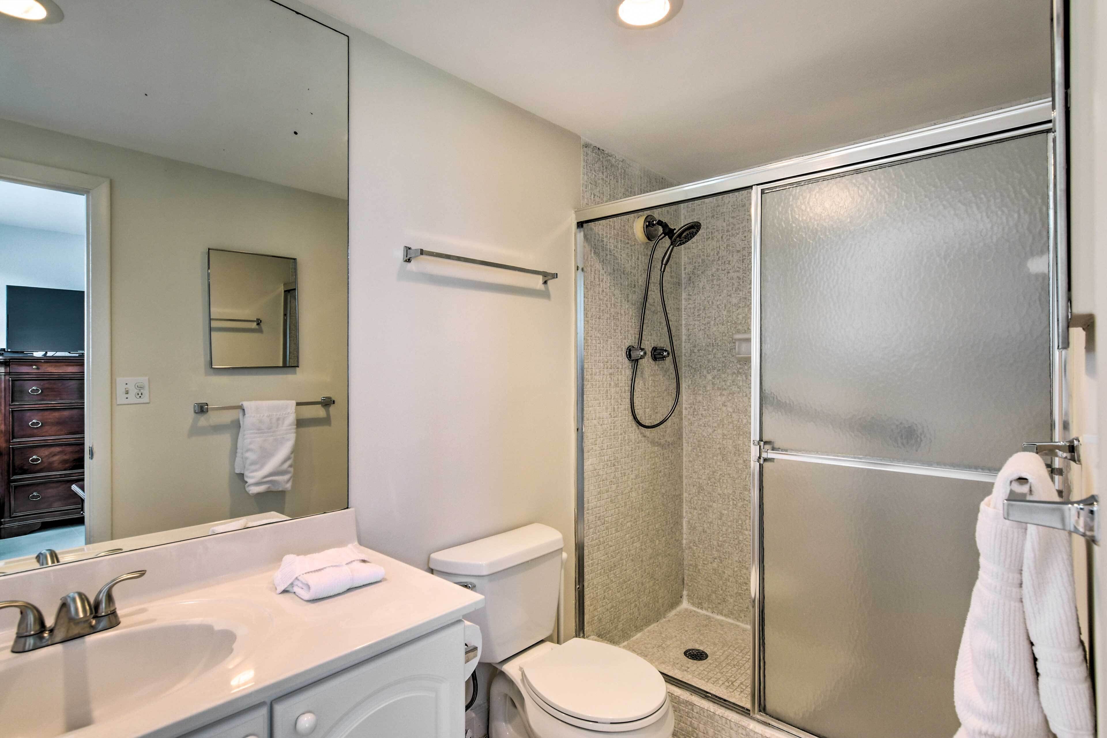 Une salle de bain moderne avec un grand miroir, un lavabo blanc, des toilettes et une douche séparée par une paroi de verre.